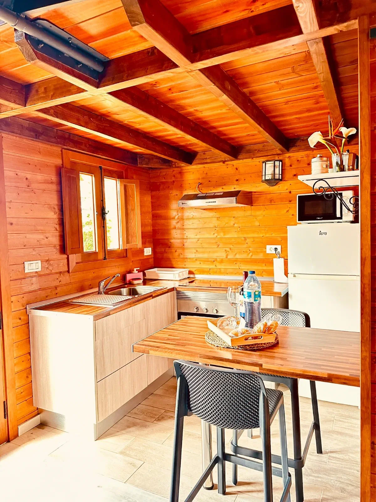 Cozy: open kitchen with fridge, microwave and a wooden high table with stools